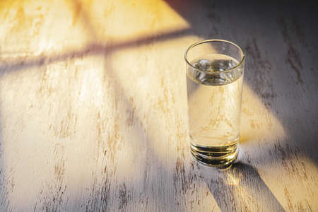 Glass of water on wooden table, sunny morning