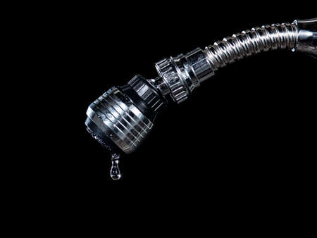 drop of water dripping from a tap isolated on black backgroundの写真素材