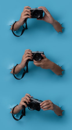 Female hand holding camera breaks through blue paper background.の写真素材