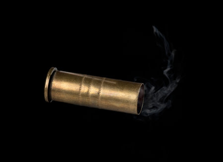 Casing fired with with smoke out of a handgun falling on black background