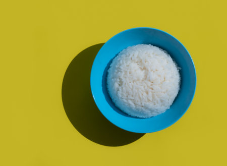 Rice in blue bowl on yellow background. The view from the top