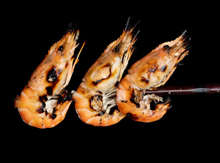 Grilled king size shrimps on wooden skewer isolated on blackの写真素材