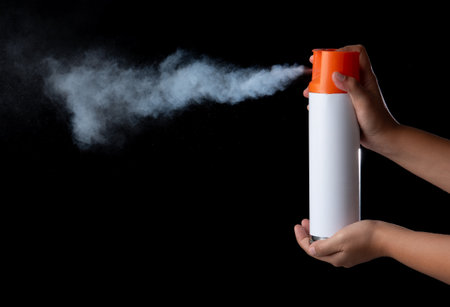 Hand holding a unlabeled white aerosol can with spray in black backの写真素材
