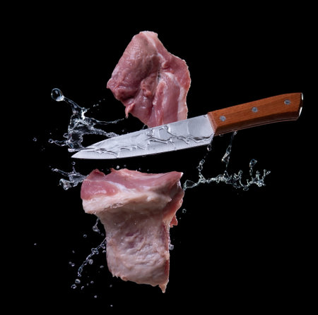 Flying pieces of pork with knife, isolated on black backgroundの写真素材