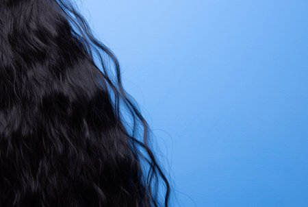 Close up of the texture of the shiny black human curly hair on the blue backgroundの写真素材