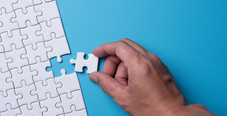Hand holding piece of white puzzle on blue background . Business strategy teamwork and problem solving concept.の写真素材