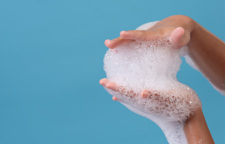 Female hand with soap bubbles on blue background. Hands with white bubbles.の写真素材