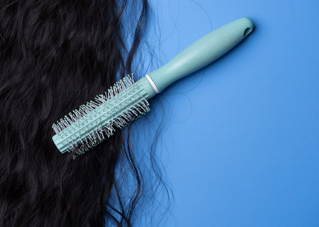 Close up of the texture of the shiny black human curly hair with comb on the blue background