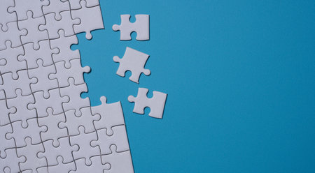 Unfinished white jigsaw puzzle on blue background with copy space. Business strategy teamwork and problem solving concept.の写真素材