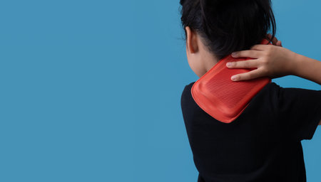 Woman putting a hot pack on her shoulder and neck pain on blue backgroundの写真素材