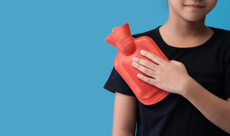 Woman putting a hot pack on her shoulder pain on blue backgroundの写真素材