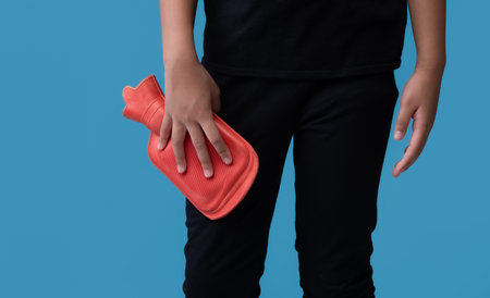 Woman using hot water bottle to leg pain on light blue backgroundの写真素材