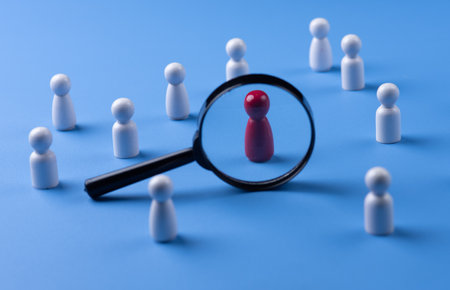 A magnifying glass and a red wooden figures with blur business man who search for someone who âs special person. Concept of Human resources management and recruitment.の写真素材