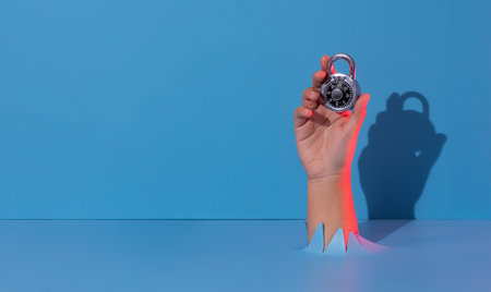 Hand holding metal lock breaks through blue paper background.の写真素材