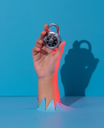 Hand holding metal lock breaks through blue paper background.の写真素材