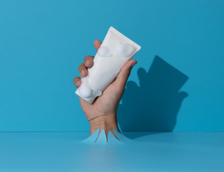 Woman with cleansing foam on hand holding tube breaks through blue paper background.の写真素材