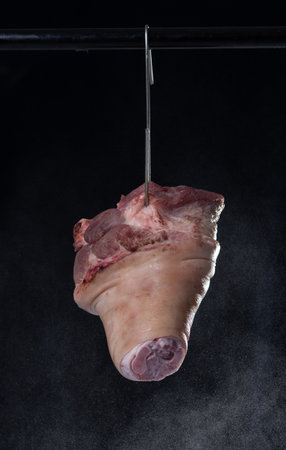 Raw pig's legs hanging on black background.の写真素材