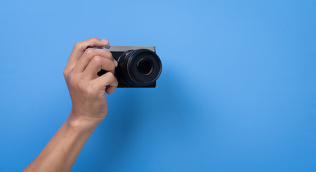 hand holding a camera with a blue backgroundの写真素材