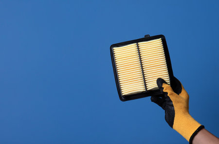Hand holding and showing new car paper air filter on blue background.の写真素材