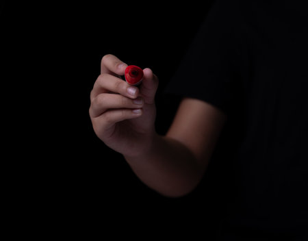 Hand holding red marker for writing on black backgroundの写真素材