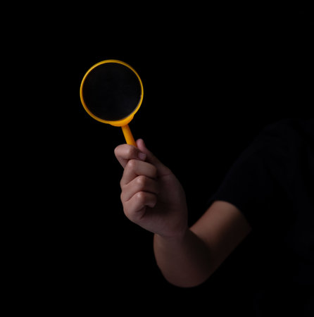 Hand Holding Magnifying Glass on Black Backgroundの写真素材