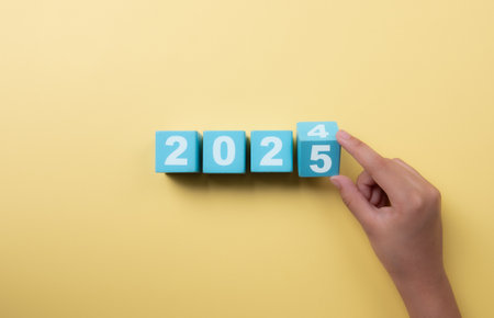 New project growth concept in 2025, Preparation for happy new year , Hand of man flip wooden cube from 2024 to 2025 on yellow background, minimal style.の写真素材