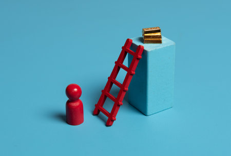 Red wooden figures with stairs and gold bars on blue background.Concept of financial goals, cunning and ingenuityの写真素材