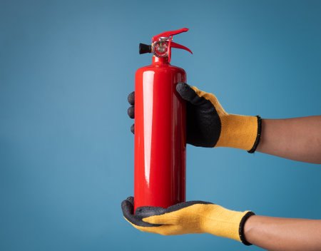 Red fire extinguisher in hand on blue backgroundの写真素材