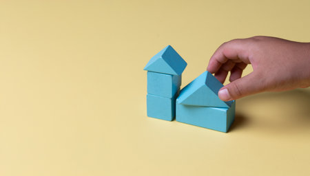 Hand building house with wooden blocks on yellow background