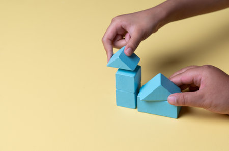 Hand building house with wooden blocks on yellow background