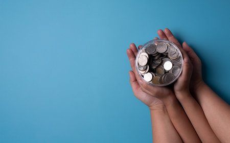 Hand holding jar of coins on a blue background.の写真素材