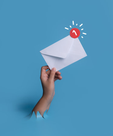 Female hand with envelope with notification red dot breaks through blue paper background.の写真素材