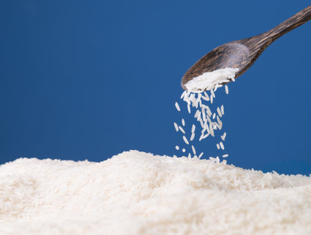 Wooden spoon pouring raw white rice against a blue backgroundの写真素材