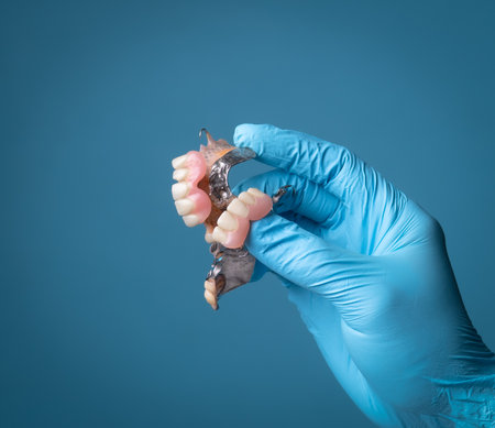 The dentist is holding dentures in his hand against a blue background