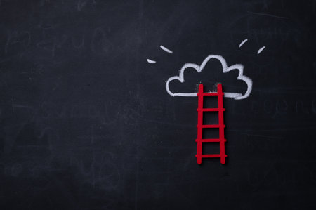 Wooden ladder leaning on blackboard with chalk drawn cloudの写真素材