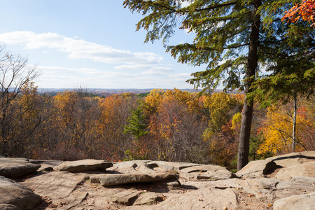 Ledges overlook in Cuyahoga Valley National Park in autumn. The fall colors are orange, yellow and red, the sky is blue with white clouds, the overlook is rock.の写真素材