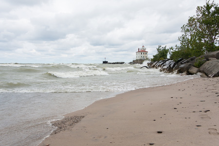 Lighthouse at Mentor Headlands Beach State Park in Ohio with waves crashing on shore and dark clouds overhead.の写真素材