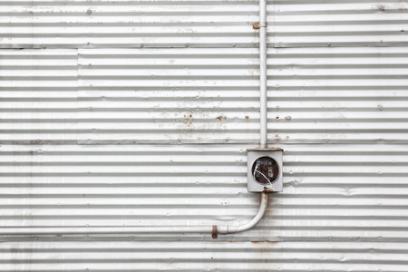 Metal piping on a corrugated metal wall leading to an electrical box with pulled out wires that are taped.の写真素材