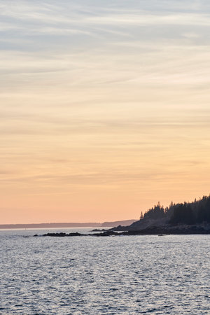 The sky is a beautiful yellow at sunset here in Acadia National Park. The rocky coastline is a...