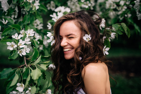 beautiful happy and smiling young brunette standing near flowering flowersの写真素材