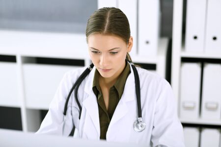 Doctor typing on pc computer while sitting at the desk in hospital office. Physician woman at work. Data in medicine and healthcareの写真素材