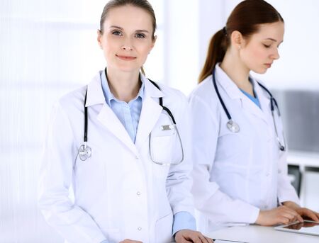 Group of doctors at work in hospital. Physician filling up medical documents or prescription while standing at reception desk. Data in medicine and health care conceptの写真素材