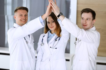 Group of modern doctors standing as a team while joining hands or giving five to each other. Physicians ready to examine and help patients. Medical help, insurance in health care, best treatment and medicine conceptの写真素材