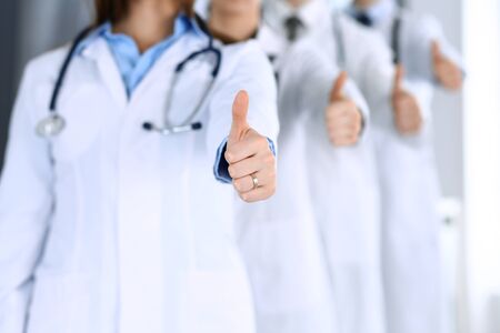 Group of modern doctors standing as a team with thumbs up in hospital office. Physicians ready to examine and help patients. Medical help, insurance in health care, best desease treatment and medicine conceptの写真素材