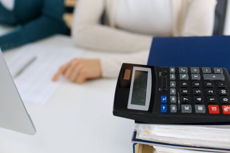 Calculator and binders with papers are waiting to be processed by business woman or bookkeeper working at the desk in office back in blur. Internal Audit and tax concept.の写真素材