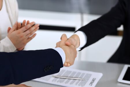 Business people shaking hands while working together at the glass desk in modern office. Unknown businessman, male entrepreneur with colleague at meeting or negotiation. Teamwork, partnership and handshake concept.の写真素材