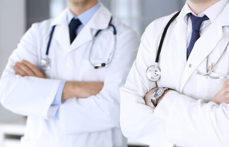 Group of modern doctors standing as a team with arms crossed in hospital office, close-up. Physicians ready to examine and help patients. Medical help, insurance in health care, best treatment and medicine concept.の写真素材