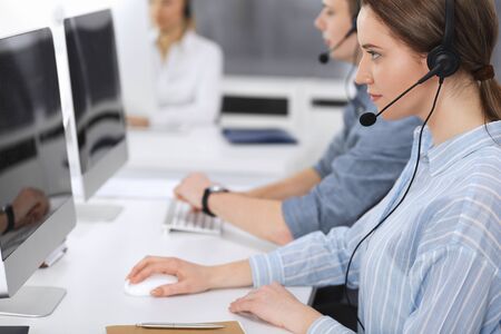 Call center. Group of casual dressed operators at work. Focus on business woman in headset at customer service office. Telesales in businessの写真素材