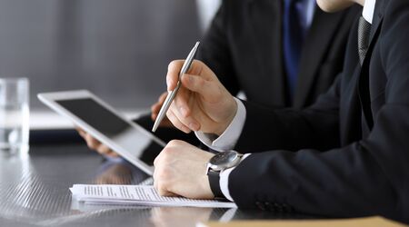 Businessman using tablet computer and work together with his colleague or partner at the glass desk in modern office, close-up. Unknown business people at meeting. Teamwork and partnership concept.の写真素材