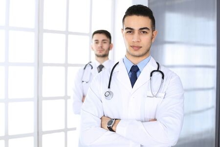 Arab doctor man standing with caucasian colleague in medical office or clinic. Diverse doctors team, medicine and healthcare conceptの写真素材
